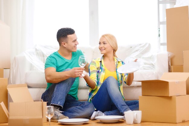 Photo moving, home and couple concept - smiling couple unpaking boxes with kitchenware in new home