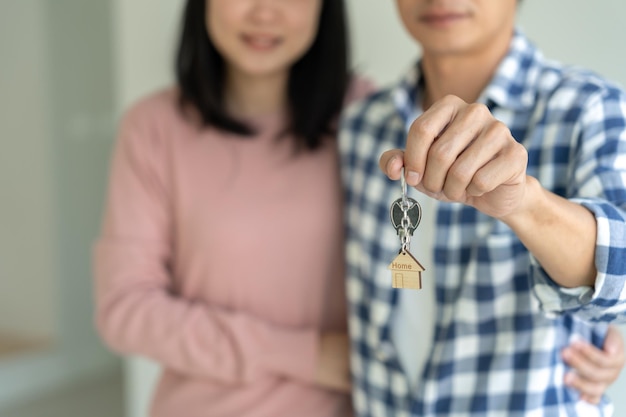 Moving house relocation Couple hold key house keychain in new apartment inside the room was a cardboard box containing personal belongings and furniture move in the new apartment or condominium