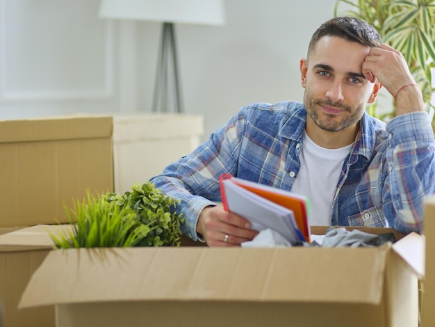 A moving man sitting on the floor in empty apartment Among the Boxes Checking the List of Things