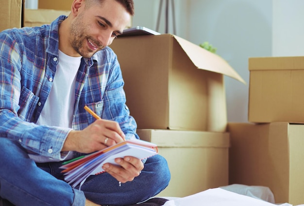 A moving man sitting on the floor in empty apartment Among the Boxes Checking the List of Things