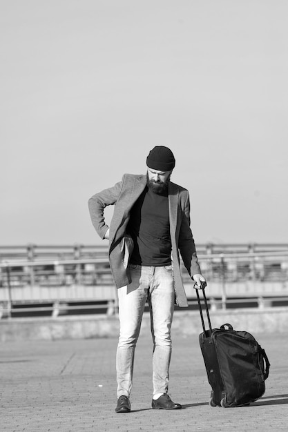 Moving to new city alone Traveler with suitcase arrive airport railway station urban background Hipster ready enjoy travel Carry travel bag Man bearded hipster travel with luggage bag on wheels