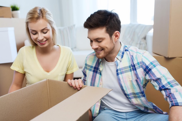 moving, people, repair and real estate concept - smiling couple looking into big cardboard box at new home