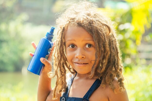 Mowgli indian boy with dreadlocks hair hiding holding mosquito\
spray in tropics green forest background