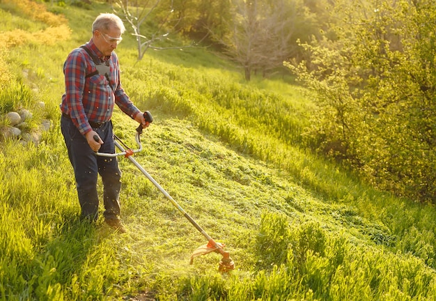 Foto decespugliatore - lavoratore che taglia l'erba nel cortile verde al tramonto.