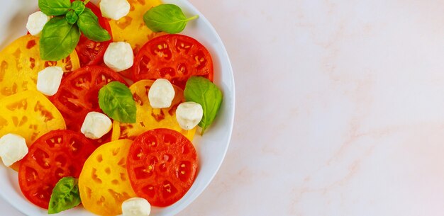 白いプレートにモッツァレラチーズ、バジル、トマト。上面図をクローズアップ。
