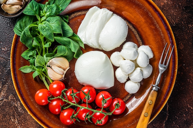 Foto mozzarella, basilico e pomodorini pronti per la cottura insalata caprese. sfondo scuro. vista dall'alto.