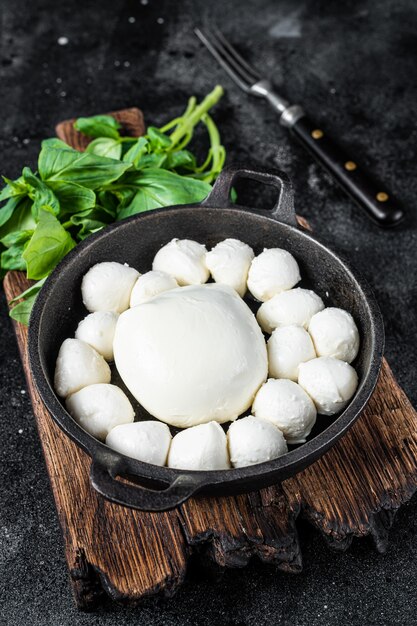 Palline di mozzarella in padella con basilico. sfondo nero. vista dall'alto.