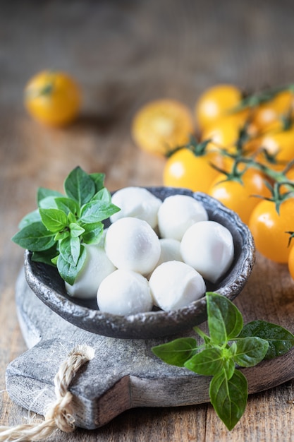 Mozzarella cheese, yellow tomatoes and basil in a ceramic bowl on a wooden board. Caprese salad ingredients. Selective focus