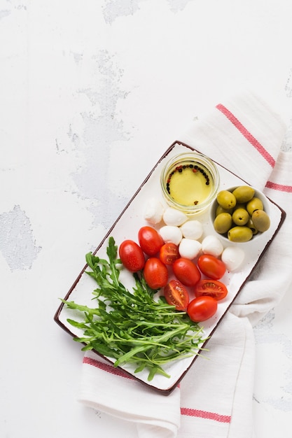 Mozzarella, cherry tomatoes and arugula served in white ceramic rectangular plates over grey texture surface. Flat lay