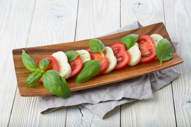Mozzarella en tomaat met basilicum bladeren op een witte houten oppervlak