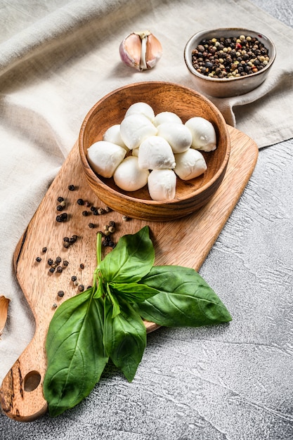 Mozzarella kaas in een houten kom met basilicum bladeren. grijze achtergrond. bovenaanzicht