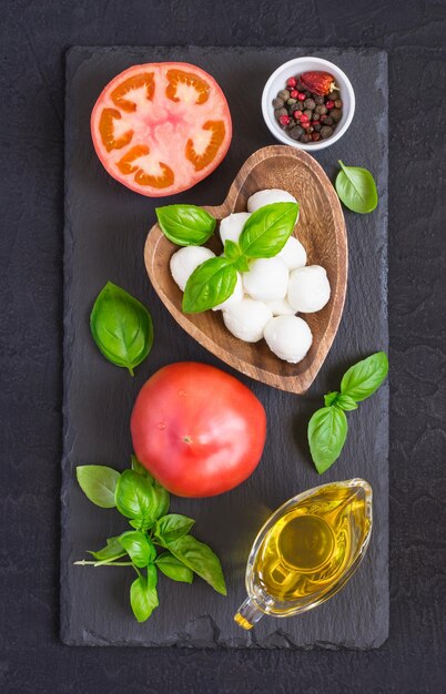 Mozzarella kaas, tomaten en basilicum op een zwarte stenen tafel. Concept van de Italiaanse keuken. Bovenaanzicht