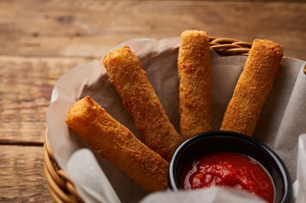 Mozzarella Sticks with ketchup dip served in a basket side view on dark background