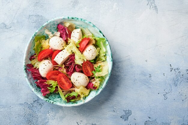 Mozzarella, tomato and mix of fresh salad leaves, slate stone table background