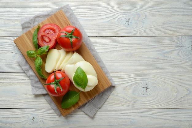 Mozzarella and tomato with basil leaves on a white wooden background