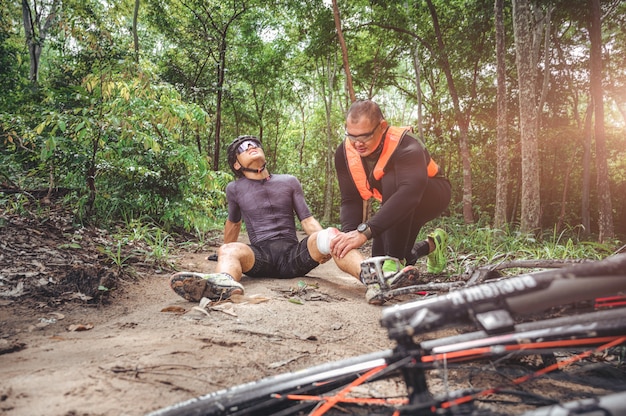 MTBマウンテンバイクの事故と応急処置：バイカーの衝突事故、膝と脚の負傷、マウンテンバイクの事故を助けるための応急処置。マウンテンバイクアスリートの応急処置チームがレース事故で負傷しました。