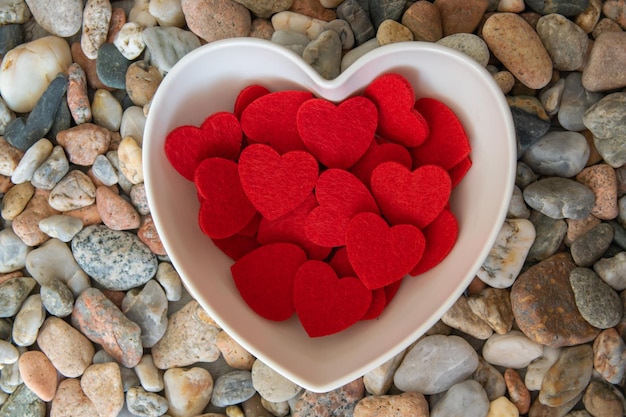 Photo much fabric red hearts in the plate on the river pebble stones