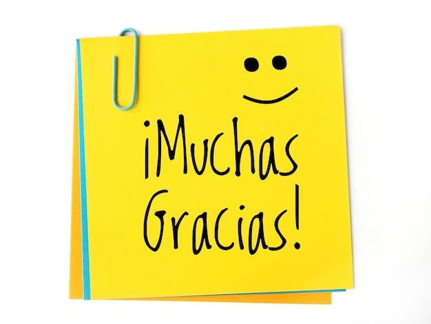 Muchas gracias handwritten on a yellow sticky note and a happy face Thank you very much in spanish