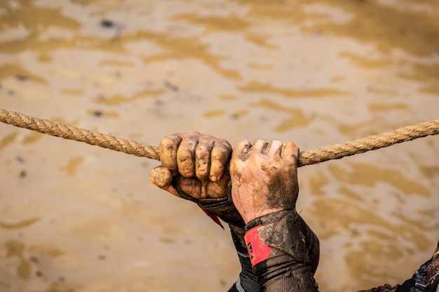 Mud race runners, defeating obstacles by using ropes. Details of the hands.