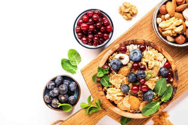 Muesli bowl and organic ingredients for healthy breakfast Granola nuts blueberry cranberry oatmeal greek yoghurt whole grain flakes on white table