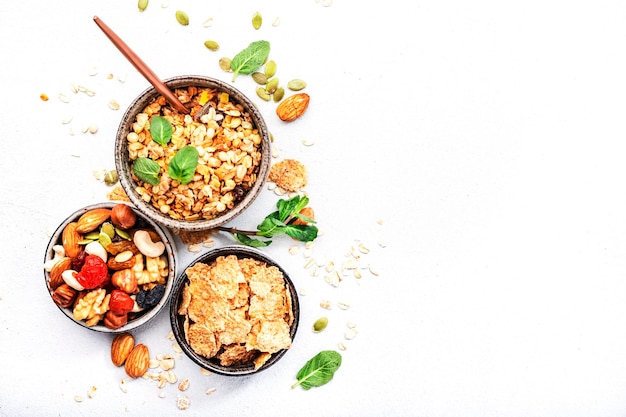 Muesli bowl and organic ingredients for healthy breakfast Granola nuts dried fruits oatmeal whole grain flakes on white table