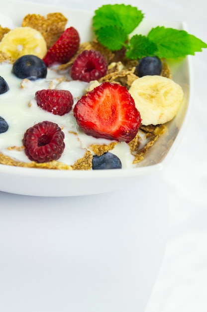 Muesli in een witte kom met fruit, banaan, framboos, aardbei, bessen