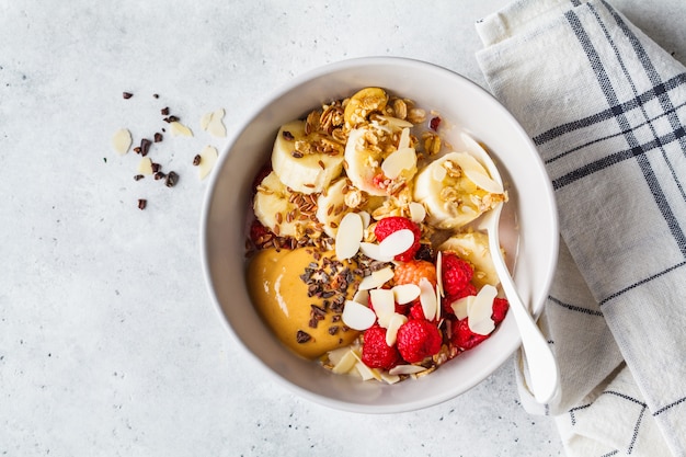 Muesli met bessen, banaan, pindakaas en chocolade in een witte kom.