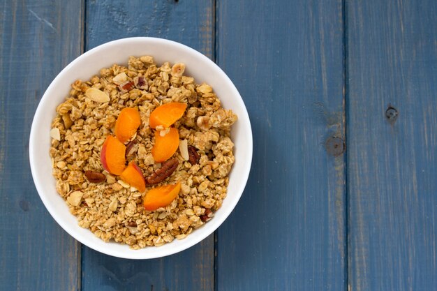 Muesli met fruit en noten in witte kom op blauwe houten oppervlak