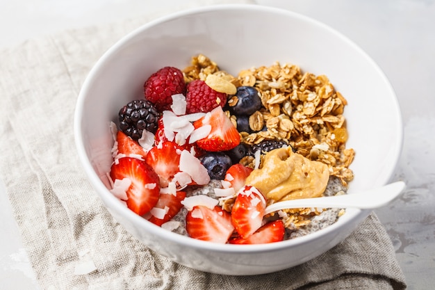 Muesli met melk, chia, bessen en pindakaas in een witte kom.