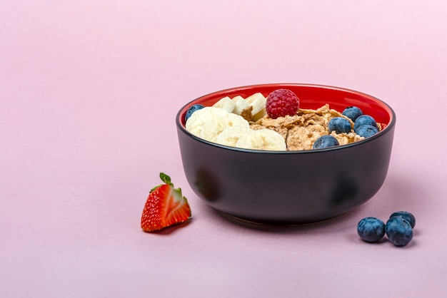 muesli. Ontbijt, gezonde voeding en dieet. Muesli met fruit in een bord op een roze achtergrond. Bosbessen, aardbeien en frambozen op een achtergrond van mueslivlokken. Print banner met kopieerruimte.