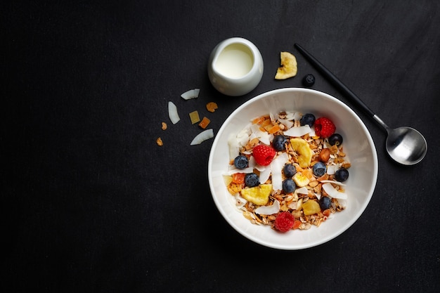 Muesli with milk served in bowl on dark background.