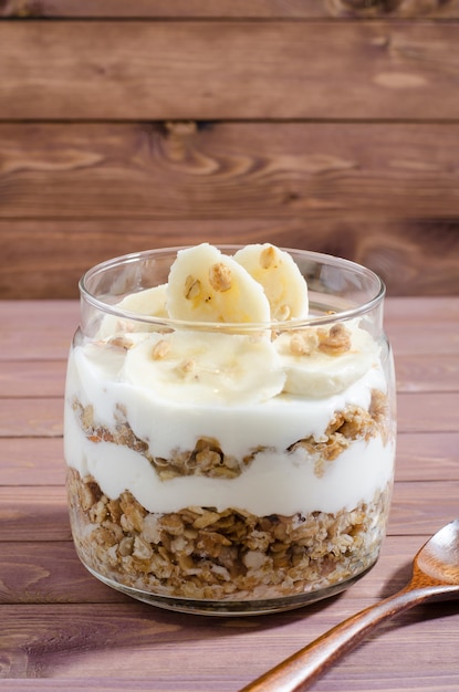 Muesli with natural yoghurt, banana, nuts and dried fruits in a glass jar