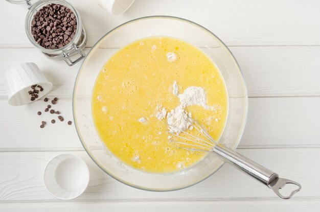 Muffin dough with chocolate chips in a bowl on a white wooden background Recipe step by step