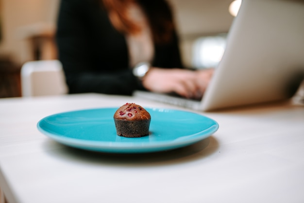 Muffin op een tartafelplaat. Detailopname. Vrouw die aan laptop op de achtergrond werkt.