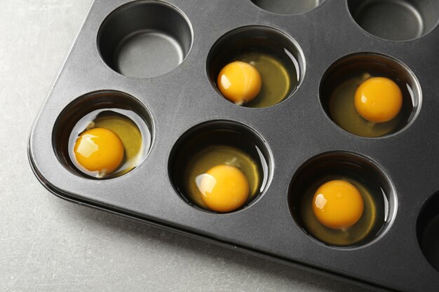 Muffin tin with raw eggs on table