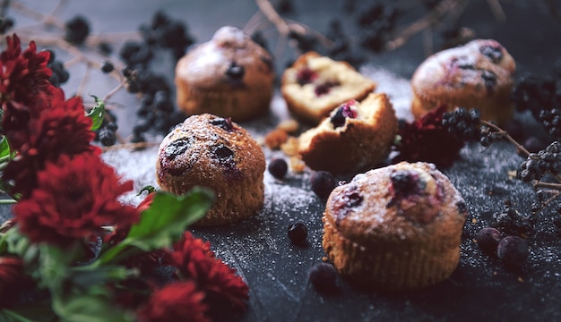 Muffin with currants on a dark background next to the berries on the branches. and a bouquet of flowers. in a rustic style. dark style