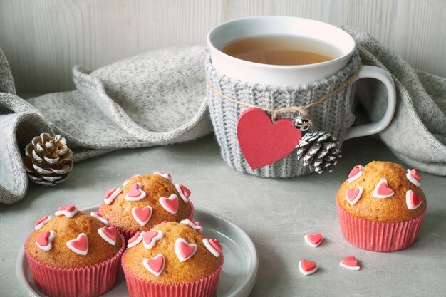 Photo muffins decorated with sugar hearts and a cup with red heart on light gray table