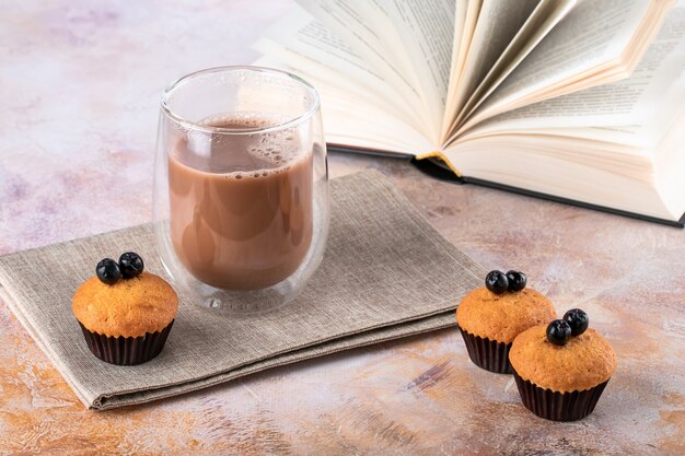 Muffins en glas witte koffie op tafel. Warme drank, cacao en open boek.