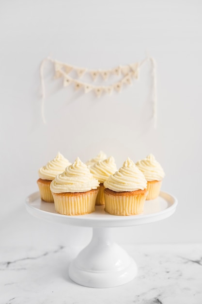 I muffin sul supporto bianco della torta contro fondo bianco