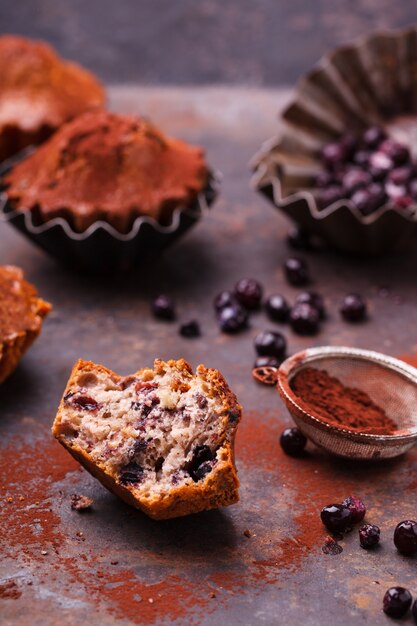 Muffins with blueberries, topped with cocoa powder, on a dark background.