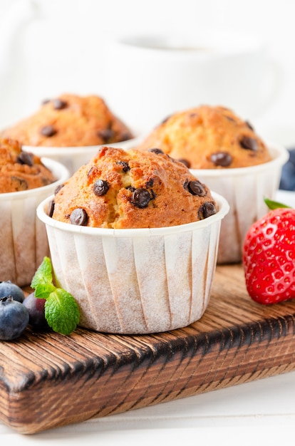 Muffins with chocolate chips on a wooden bord on a white background with fresh berries. Copy space.