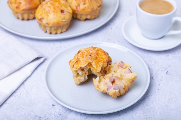 Muffins with ham and cheese. Homemade baking. In the background is a plate with muffins and a cup of coffee. Close-up.