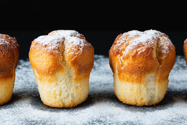 Muffins with white powdered sugar on black background