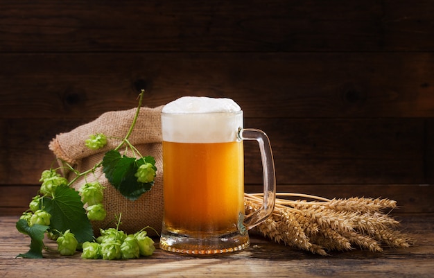 Mug of beer with green hops and wheat ears on wooden table