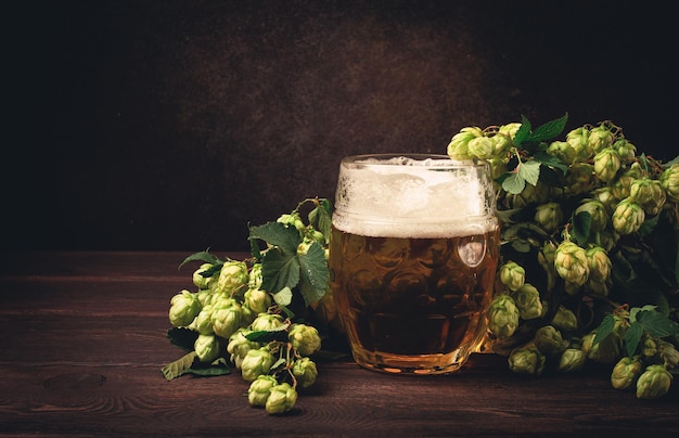 A mug of beer on a wooden table with a branch of fresh hops rustic no people