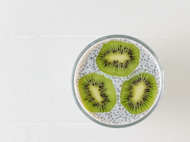 A mug of black Chia seed pudding and three kiwi slices on a white table. The view from the top. Flat lay.