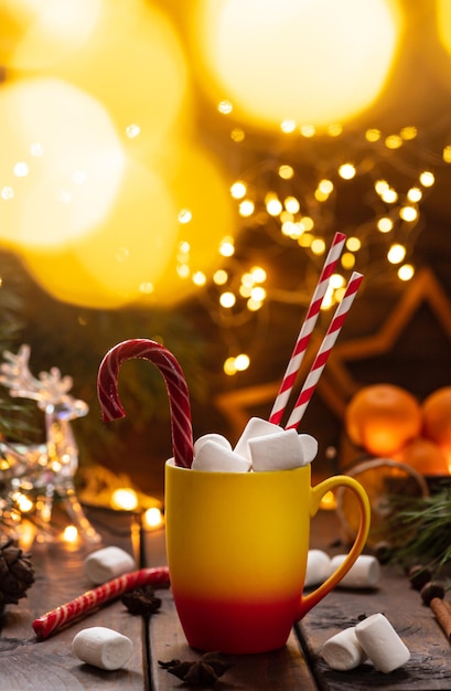 A mug of cocoa with marshmallows from which straws stick out, a caramel stick