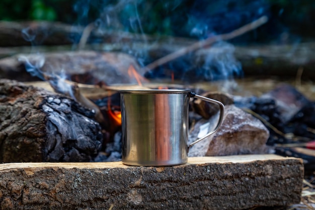 A mug of coffee sits on a fire in front of a campfire.