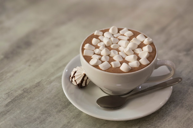 Mug of coffee with marshmallows on porcelain plate on light background