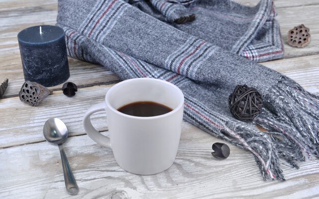 Mug of coffee with scarf and candle  on a table